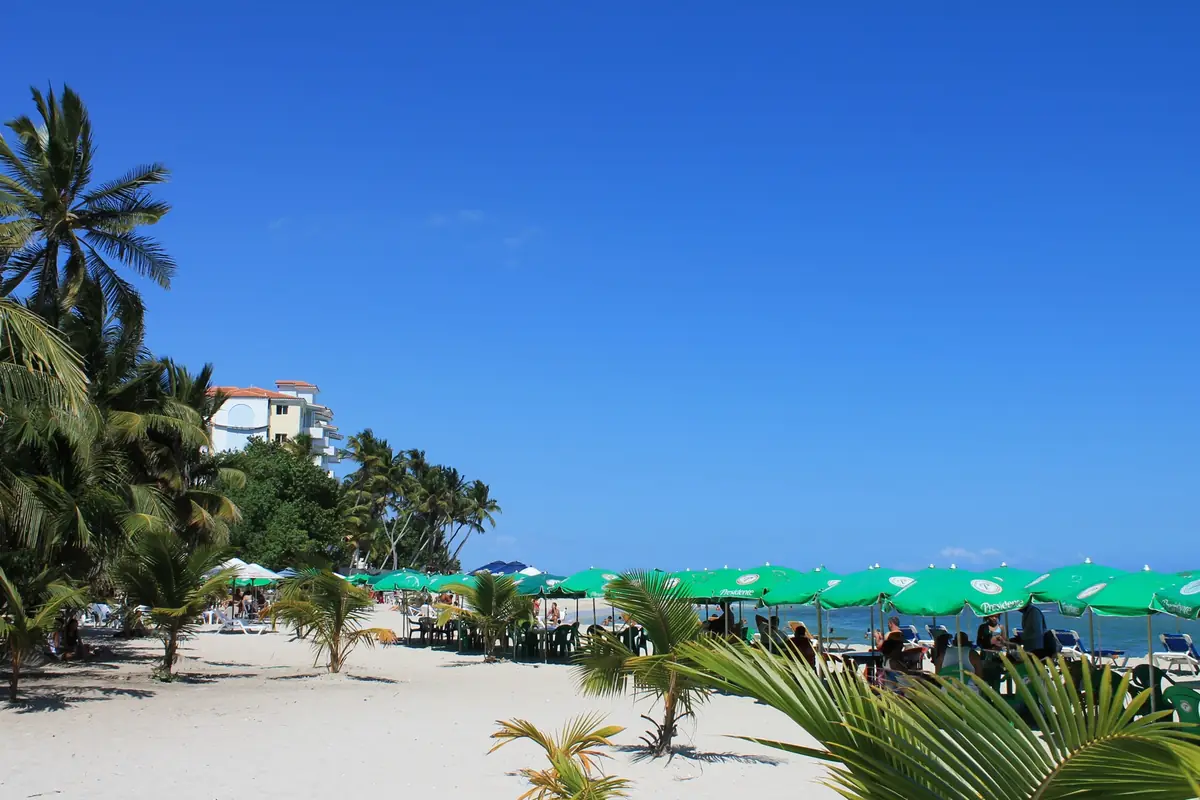 Arena blanca, palmeras y sombrillas en la playa pública de Juan Dolio
